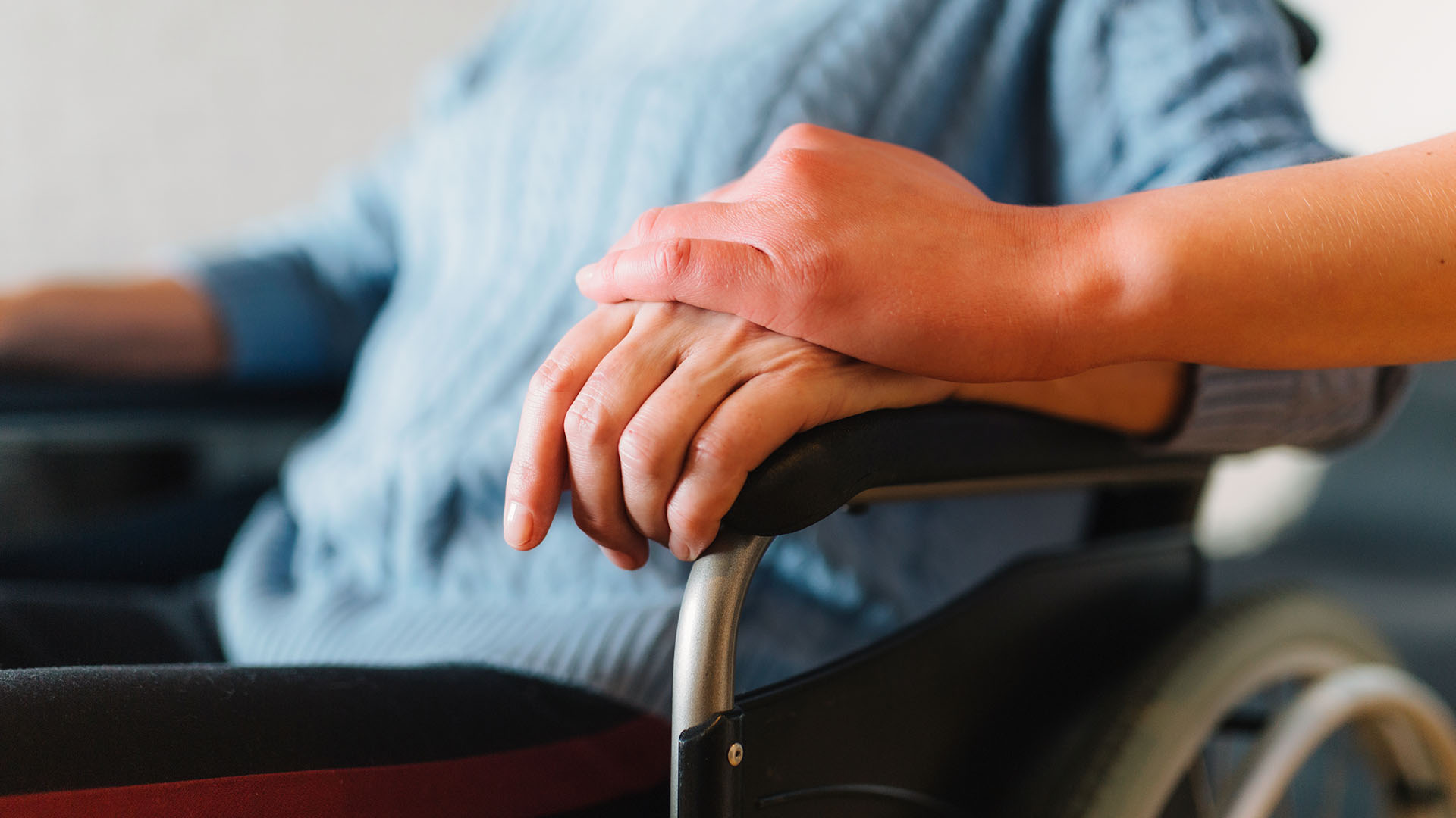 Fürsorgliche Hand auf der Hand eines Seniors im Rollstuhl